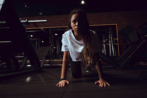 attractive african american woman with dreadlocks doing plank exercise in gym 
