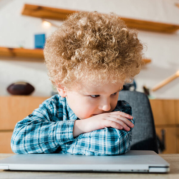 задумчивый и умный ребенок сидит рядом с ноутбуком
 