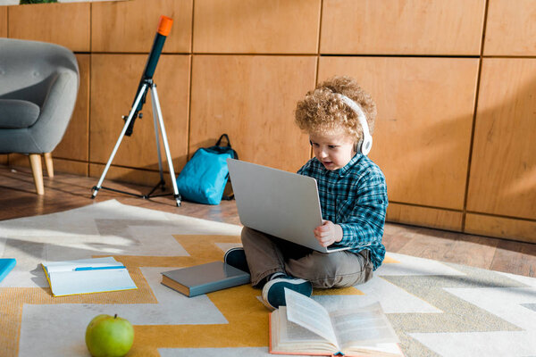 smart child in headphones using laptop near apple and books 