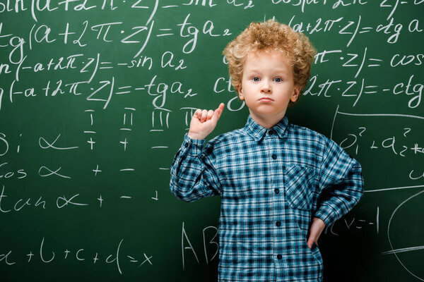 smart kid standing with hand on hip near chalkboard with mathematical formulas 