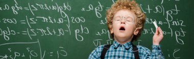 panoramic shot of curly kid in glasses sneezing near chalkboard with mathematical formulas  clipart