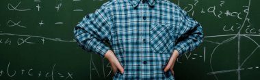 panoramic shot of smart kid standing with hands on hips near chalkboard  clipart
