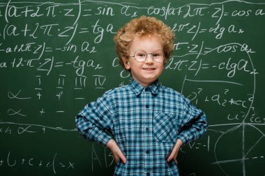 happy kid in glasses standing with hands on hips near chalkboard  clipart