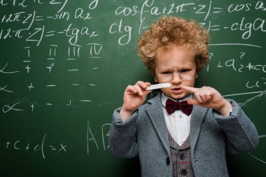 Matematiksel formüllerle tebeşiri işaret eden papyonlu akıllı çocuk. 