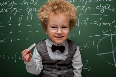 Matematiksel formüllü tebeşir tutan takım elbiseli ve papyonlu akıllı çocuk. 