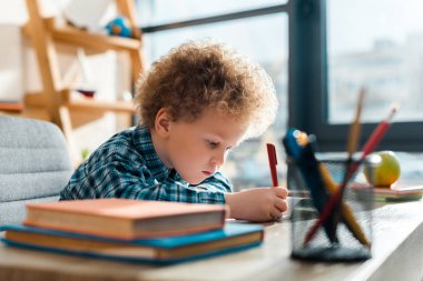 selective focus of curly kid writing near books  clipart