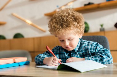 smart child writing in notebook near books on table  clipart