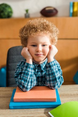 smart child looking at camera near books on table  clipart