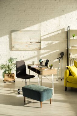 Living room with laptop on table and crutches near wall clipart