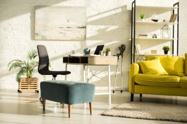 Sunlit living room with laptop on table and crutches near wall