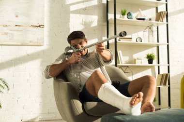 KYIV, UKRAINE - JANUARY 21, 2020: Handsome man with broken leg fooling around with crutch in living room