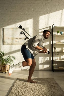 Side view of handsome smiling man holding crutches in living room