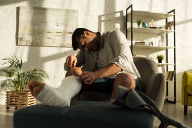 Handsome man scratching broken leg with ruler at home