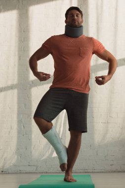 Man with neck brace and broken leg training on fitness mat at home