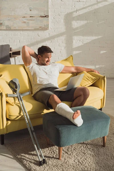 Smiling Man Broken Leg Ottoman Looking Laptop Sofa Home — Stockfoto