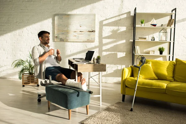 Glimlachende Man Met Gebroken Beker Aan Tafel Met Laptop — Stockfoto