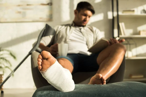 Selektywne Skupienie Człowieka Nogą Gipsowym Bandażu Trzymając Kubek Książkę Czytania — Zdjęcie stockowe