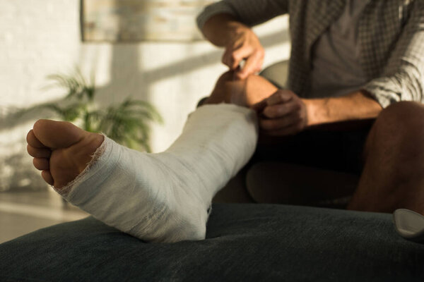 Selective focus of man scratching broken leg with ruler while sitting in armchair