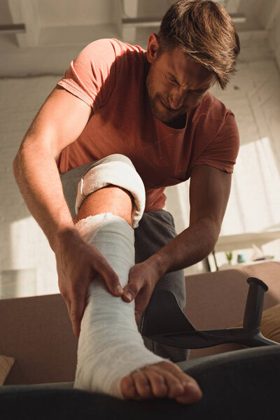 Low angle view of man with broken leg having pain at home