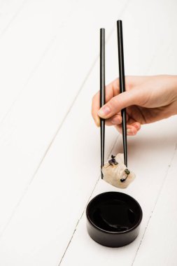 cropped view of woman eating delicious Chinese boiled dumpling with chopsticks and soy sauce at white wooden table