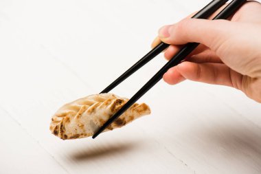 cropped view of woman eating delicious gyoza with chopsticks at white wooden table