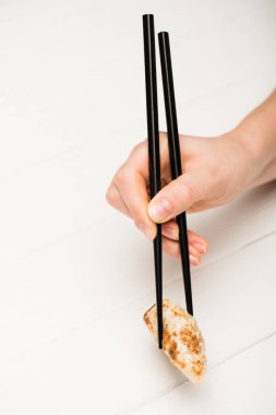 cropped view of woman eating delicious gyoza with chopsticks at white wooden table