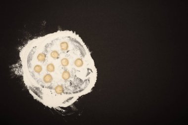 top view of raw dough balls for dumplings on flour on black background