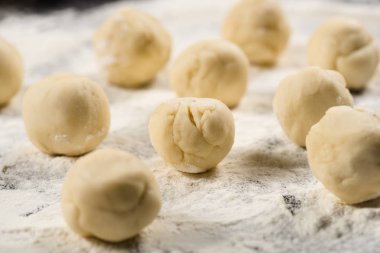 close up view of raw dough balls for dumplings on flour
