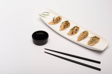 delicious gyoza on plate near chopsticks and soy sauce on white background