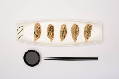 top view of delicious gyoza on plate near chopsticks and soy sauce on white background