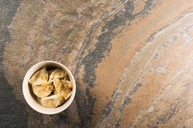 top view of delicious varenyky with fried onion in bowl on stone surface