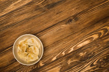 top view of delicious varenyky with fried onion in bowl on wooden table