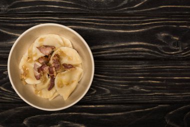 top view of delicious varenyky with cracklings in bowl on black wooden table