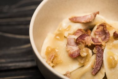 close up view of delicious varenyky with cracklings in bowl on black wooden table