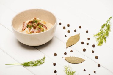 delicious varenyky with cracklings and dill in bowl near bay leaves and black peppercorns on white wooden table