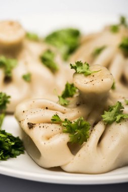 close up view of delicious Khinkali with cilantro and black pepper on white plate