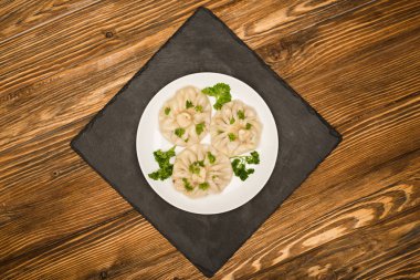 top view of delicious Khinkali with cilantro on plate on brown wooden table clipart