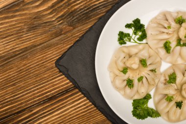 top view of delicious Khinkali with cilantro on plate on brown wooden table