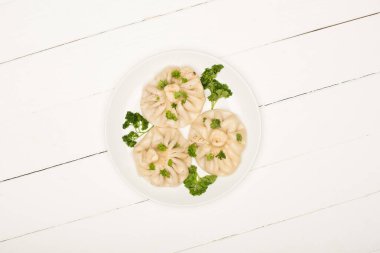 top view of delicious Khinkali with cilantro on plate on white wooden table