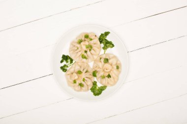 top view of delicious Khinkali with cilantro on plate on white wooden table clipart