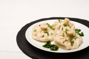 delicious Khinkali with cilantro on plate on white wooden table