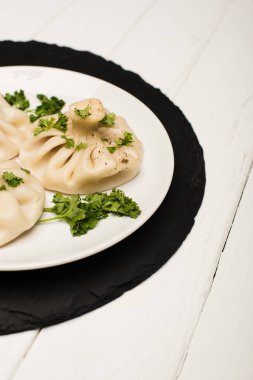 close up view of delicious Khinkali with cilantro on plate on white wooden table