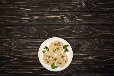 top view of delicious Khinkali with cilantro on plate on black wooden table