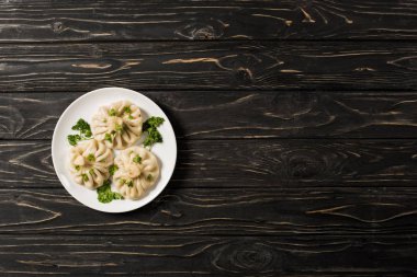 top view of delicious Khinkali with cilantro on plate on black wooden table