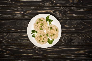 top view of delicious Khinkali with cilantro on plate on black wooden table