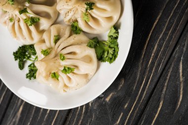top view of delicious Khinkali with cilantro on plate on black wooden table