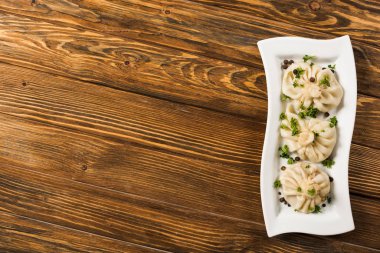top view of delicious Khinkali with cilantro on plate on brown wooden table