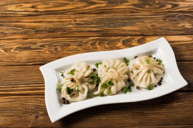 top view of delicious Khinkali with cilantro on plate on brown wooden table