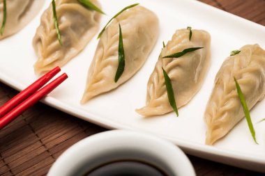 close up view of delicious Chinese boiled dumplings on plate near chopsticks and soy sauce on bamboo mat