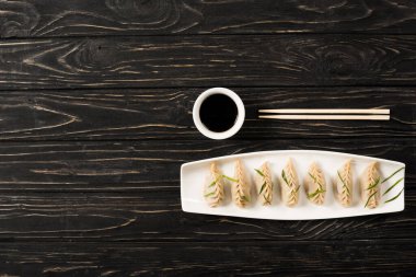 top view of delicious Chinese boiled dumplings on plate near chopsticks and soy sauce on black wooden table